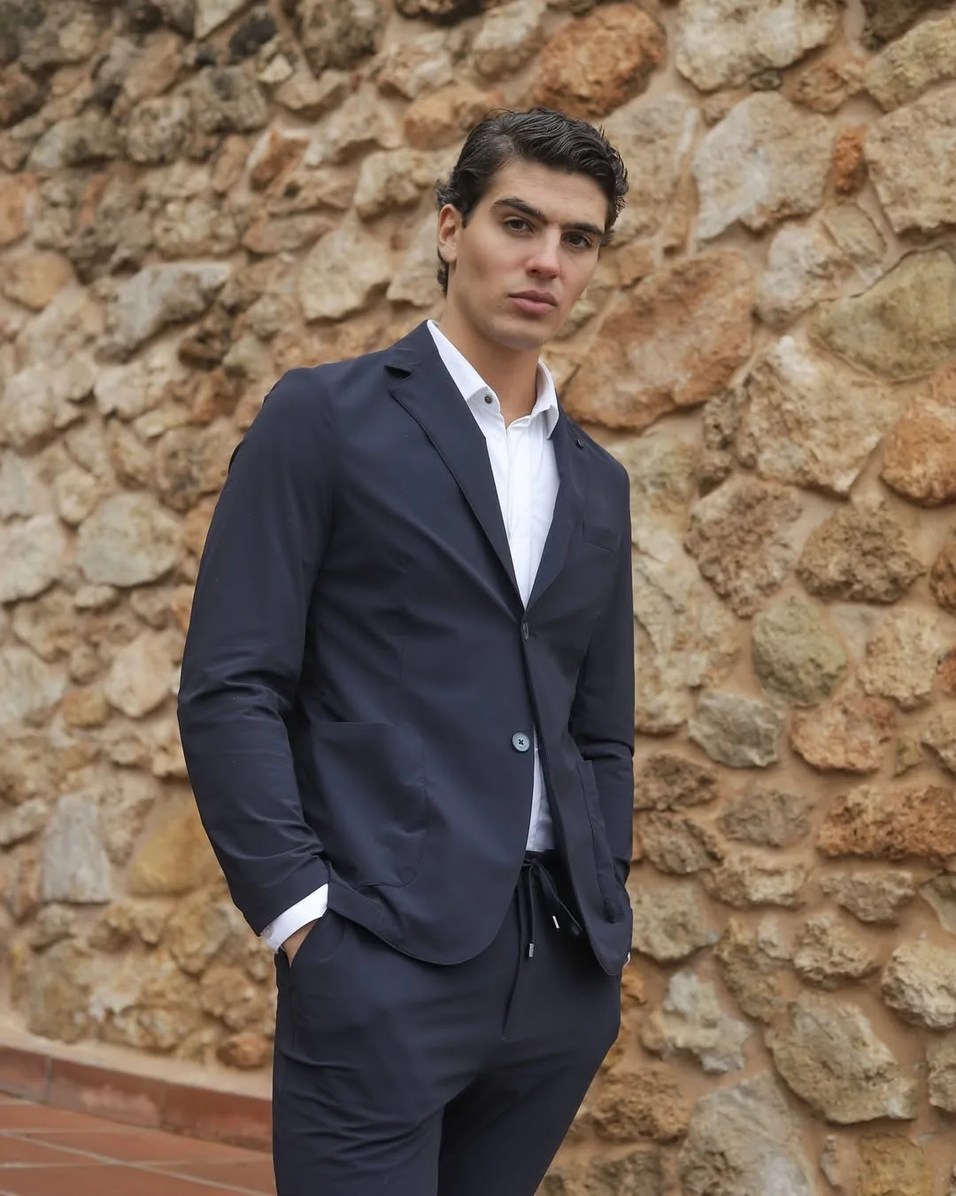 Hombre con traje Active azul y camisa blanca frente a una pared de piedra